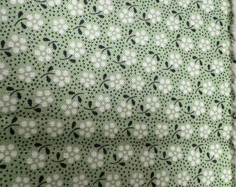 May include: Close-up of a green fabric with a repeating pattern of white floral shapes and black leaf accents. The fabric has a textured appearance, with a subtle grid-like structure. The overall design is reminiscent of a vintage or cottagecore aesthetic.