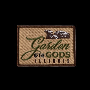 May include: A brown and tan embroidered patch with the text "Garden of the Gods Illinois" in green and black lettering. The patch features a brown and white image of a rock formation.