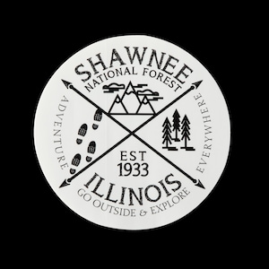 May include: Black and white graphic design of a logo for the Shawnee National Forest in Illinois. The logo features a compass with the words "Shawnee National Forest" and "Illinois" in a circle. The compass points are labeled "Adventure" and "Everywhere". The logo also includes a mountain range, footprints, and a group of trees.