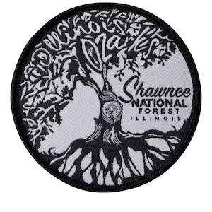 May include: White embroidered patch with a black outline. The patch features a stylized tree with the text "Shawnee National Forest Illinois" and the words "The Woods Are Calling" written around the tree.