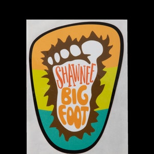 May include: A sticker with a brown footprint with the text "SHAWNEE BIG FOOT" in orange, yellow, and teal colors.