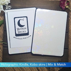May include: Two rectangular e-reader skins with rounded corners. One skin features a white background with a black logo displaying a crescent moon, stars, and the text Bookish Decals Handmade With Love. The other skin has a holographic finish.