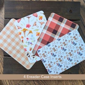 May include: Four eReader case inserts with various patterns. Designs include a peach gingham, mushrooms and flowers, a red and brown plaid, and a light blue pattern with bows and leaves. The inserts are arranged on a dark wooden surface.