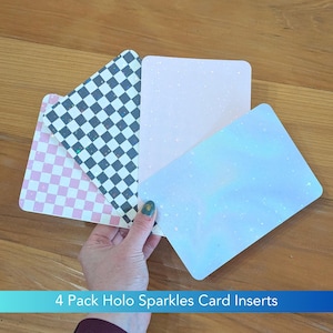May include: A set of four rectangular card inserts featuring holographic sparkle finishes. The designs include a pink and white checkerboard pattern, a black and white checkerboard pattern, a solid light pink, and a solid light blue card.