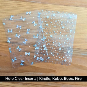 Peut inclure: Deux inserts rectangulaires en plastique transparent avec des motifs holographiques. L'un présente un motif répétitif de petits nœuds, l'autre un motif dense d'étoiles de tailles variées. Le texte en bas indique : Holo Clear Inserts | Kindle, Kobo, Boox, Fire.