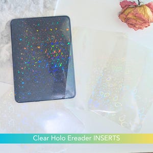 Puede incluir: Insertos transparentes para lectores electrónicos holográficos con un fondo oscuro y un diseño brillante y colorido. Los insertos son rectangulares y tienen una capa transparente. El texto "Clear Holo Ereader INSERTS" está en la parte inferior.