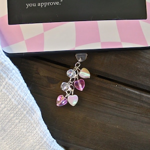 May include: A pink and white checkered e-reader with a charm attached to the bottom. The charm is a silver chain with pink and iridescent heart-shaped beads.