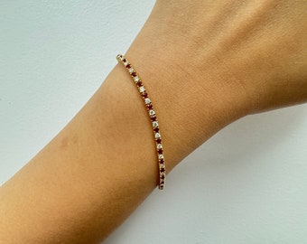 May include: A gold tennis bracelet with alternating red and white gemstones.