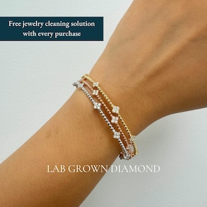 May include: A set of three thin bracelets in yellow, rose, and white gold tones, each featuring a series of small, four-petaled flower motifs set with lab-grown diamonds. The text "LAB GROWN DIAMOND" is visible at the bottom of the image.