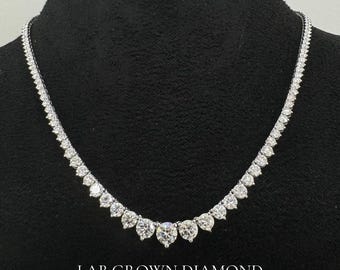 May include: A silver necklace with a row of round, clear lab-grown diamonds. The diamonds are set in a graduated pattern, with the largest diamonds in the center of the necklace. The necklace is on a black background. "LAB GROWN DIAMOND" is written in white text at the bottom of the image.