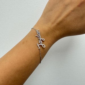 May include: A silver bracelet with the name "Jennifer" spelled out in small diamonds.