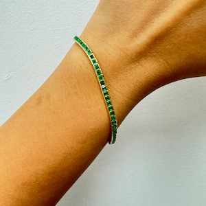 May include: A gold bracelet with a row of emerald green square-shaped stones.