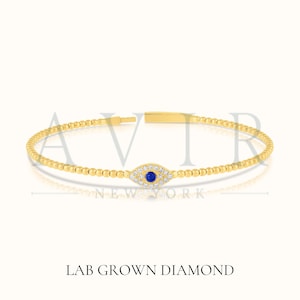 May include: A gold-colored bracelet with a beaded design. The bracelet features an eye-shaped charm with a blue center stone and surrounding white stones. The text "LAB GROWN DIAMOND" is at the bottom of the image.