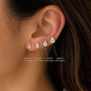 May include: Four pear-shaped stud earrings in gold settings, arranged by size on an earlobe. Text labels indicate total weights of 0.50 CT, 1.00 CT, 1.50 CT, and 2.00 CT. Each earring features a clear, faceted stone held by a small metal prong setting.