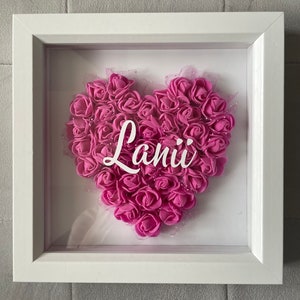 May include: A white frame containing a pink heart made of artificial roses. The name "Lani" is written in white letters inside the heart.