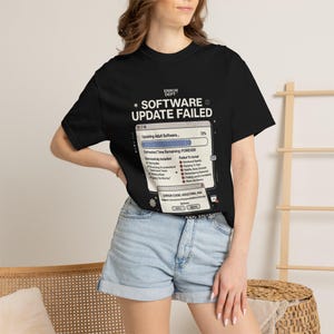 Könnte beinhalten: Ein schwarzes T-Shirt mit einem Grafikdruck eines Computerfensters mit der Aufschrift "SOFTWARE UPDATE FAILED". Das Design enthält einen Fortschrittsbalken, eine Liste mit "Successfully Installed" und "Failed To Install" Aufgaben.