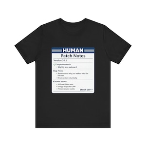 May include: A black short-sleeve t-shirt featuring a white rectangular graphic labeled HUMAN Patch Notes Version 26.1. The text lists Improvements, Bug Fixes including remembered why you walked into the kitchen, and Known Issues like printer remains hostile.