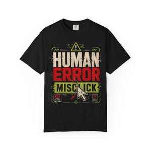Puede incluir: Una camiseta negra de manga corta con un diseño gráfico que incluye el texto HUMAN ERROR MISCLICK. El diseño presenta un triángulo de advertencia amarillo, un icono de cursor de ordenador agrietado y recuadros con 404 INTENT NOT FOUND y OOPS AGAIN.