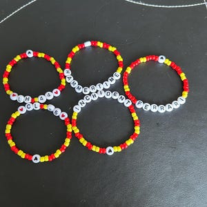 Peut inclure: Quatre bracelets en perles rouges et jaunes avec des perles de lettres blanches qui épellent "HAMMERTIME", "INCIDENT", "LH44" et "FERRARI".