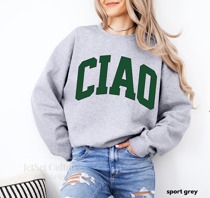 May include: A gray sweatshirt with the word "CIAO" printed in green letters. The sweatshirt is being modeled by a person wearing blue jeans.