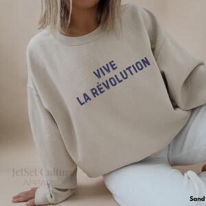 May include: A beige sweatshirt with the text "VIVE LA R&Eacute;VOLUTION" printed in blue on the front.
