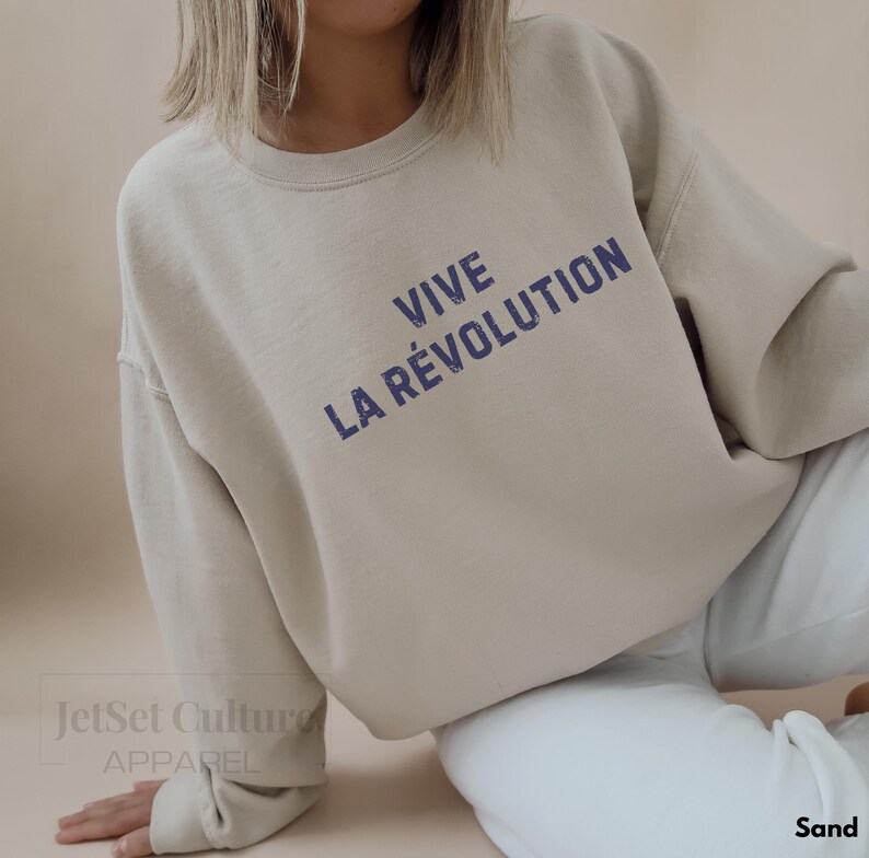 May include: A beige sweatshirt with the text "VIVE LA R&Eacute;VOLUTION" printed in blue on the front.