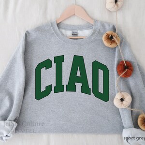May include: A gray sweatshirt with the word "CIAO" printed in green letters on the front. The sweatshirt is a classic crew neck style.