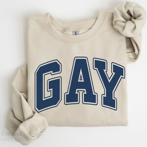 May include: A beige sweatshirt with the word "GAY" printed in navy blue block letters.