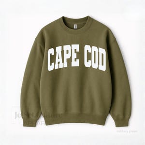May include: Olive green sweatshirt with the white text "CAPE COD" across the chest. The sweatshirt is a crew neck style and has long sleeves. The words "military green" are printed on the bottom right corner.