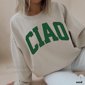 May include: A beige sweatshirt with the word "CIAO" printed in green letters in an arched style.