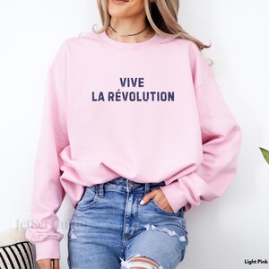 May include: A light pink sweatshirt with the text "VIVE LA R&Eacute;VOLUTION" printed in dark blue.