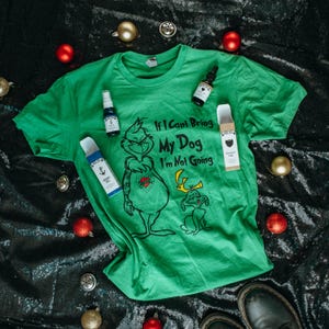 May include: A green t-shirt with a graphic of a Grinch-like character and the text "If I Can't Bring My Dog I'm Not Going." The image also includes small bottles and Christmas ornaments.