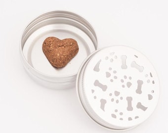 Può includere: Un contenitore in metallo argentato con un dolcetto per cani a forma di cuore all'interno. Il coperchio del contenitore ha un design di impronte di zampe e ossa.