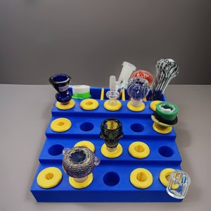 May include: Blue and yellow storage organizer with multiple compartments for holding glass and ceramic smoking accessories.
