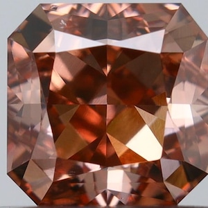 May include: A square-cut gemstone with a deep reddish-brown hue and a brilliant faceted surface. The stone displays a symmetrical arrangement of triangular and trapezoidal facets that reflect light, creating a complex pattern of dark and light tones.