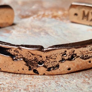Peut inclure: Un bracelet en cuivre avec une finition texturée et martelée. Le bracelet a une forme simple et arrondie et est marqué des lettres "M.X.S."
