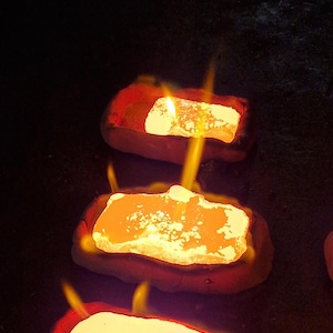May include: Close-up of three glowing, rectangular objects with flames. The objects have a bright yellow-orange center and a red border, set against a dark background. The flames are yellow and orange.