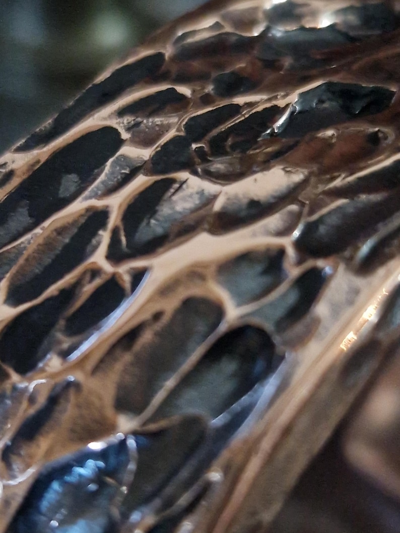 May include: Close-up of a textured, metallic surface with a honeycomb-like pattern. The surface has a bronze color with dark, irregular openings, reflecting light and creating shadows. The overall effect is of a detailed, organic design.