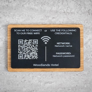 Könnte beinhalten: Rechteckiges Schild mit Holzrahmen und schwarzem Mittelteil. Das Schild zeigt einen QR-Code, ein Wi-Fi-Symbol und den Text "SCAN ME TO CONNECT TO OUR FREE WIFI!" und "Woodlands Hotel."