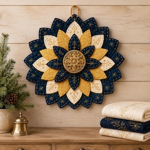 May include: A circular wall hanging featuring layered fabric petals in navy blue, mustard yellow, and cream with intricate gold embroidery. A central gold medallion with a floral relief design sits at the core. A braided cord loop is attached at the top.