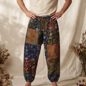 May include: A short-sleeved, cream-colored crew neck t-shirt paired with loose-fitting, ankle-length trousers featuring a patchwork design. The trousers display a multi-colored pattern of various mushrooms and botanical elements on dark fabric panels.