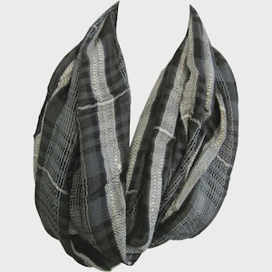 May include: A black, gray, and white infinity scarf with a plaid and herringbone pattern. The scarf is made of a soft, lightweight material and is designed to be worn looped around the neck. The scarf is a versatile accessory for any wardrobe.