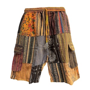 May include: Patchwork shorts with a drawstring waist. The shorts feature a variety of colourful fabric patches in shades of orange, yellow, brown, and blue. The design includes pockets and decorative stitching.
