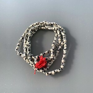 May include: White and black beaded necklace with a red tassel. The beads are cylindrical and have a skull pattern.