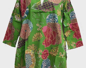 May include: A green tunic with a V-neck and long sleeves. The tunic is adorned with a vibrant floral pattern in shades of pink, yellow, blue, and brown. The design features large, stylized flowers and circular motifs, creating a bold and colorful look.