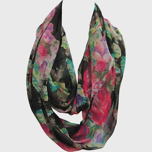 May include: An infinity scarf with a floral pattern. The scarf features a black background with a colorful design of pink, purple, green, and blue flowers. The scarf is made of a lightweight material.