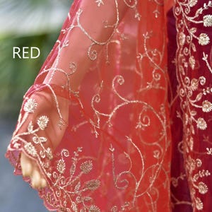 May include: Red sheer fabric with detailed gold embroidery. The fabric is draped, displaying delicate floral and swirling patterns. The word "RED" is visible in the upper left corner. The overall effect is elegant and ornate.