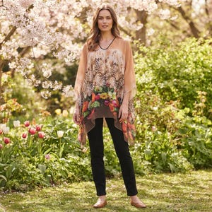 May include: A sheer, peach-colored poncho featuring a dark animal print pattern on the upper section and a vibrant floral print along the bottom hem, paired with solid black slim-fit trousers and simple tan flat shoes.