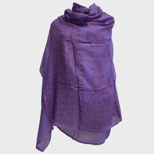 May include: A draped, purple shawl with a detailed, repeating pattern in a darker shade of purple. The design includes figures and script. The fabric appears soft and lightweight, suitable for layering or draping.