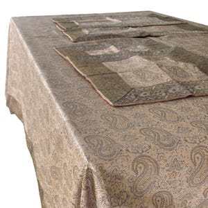 May include: A beige paisley tablecloth with matching placemats. The tablecloth and placemats have a repeating paisley pattern in shades of beige, gray, and gold. The placemats have a dark green border.